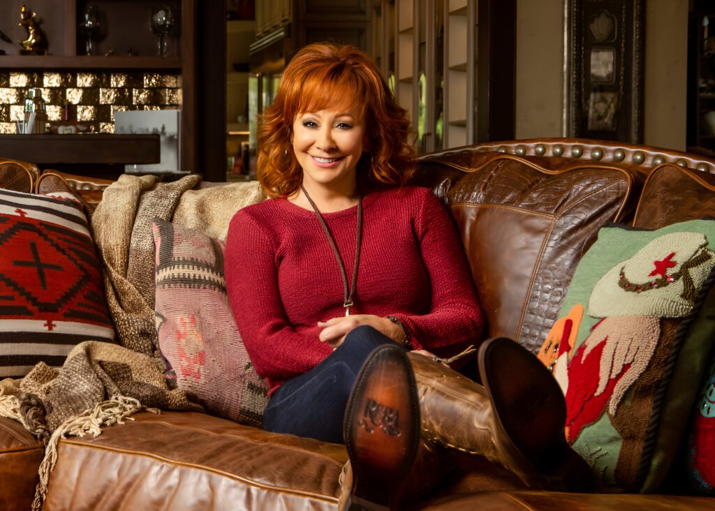 Reba McEntire sitting in sofa wearing her branded products.